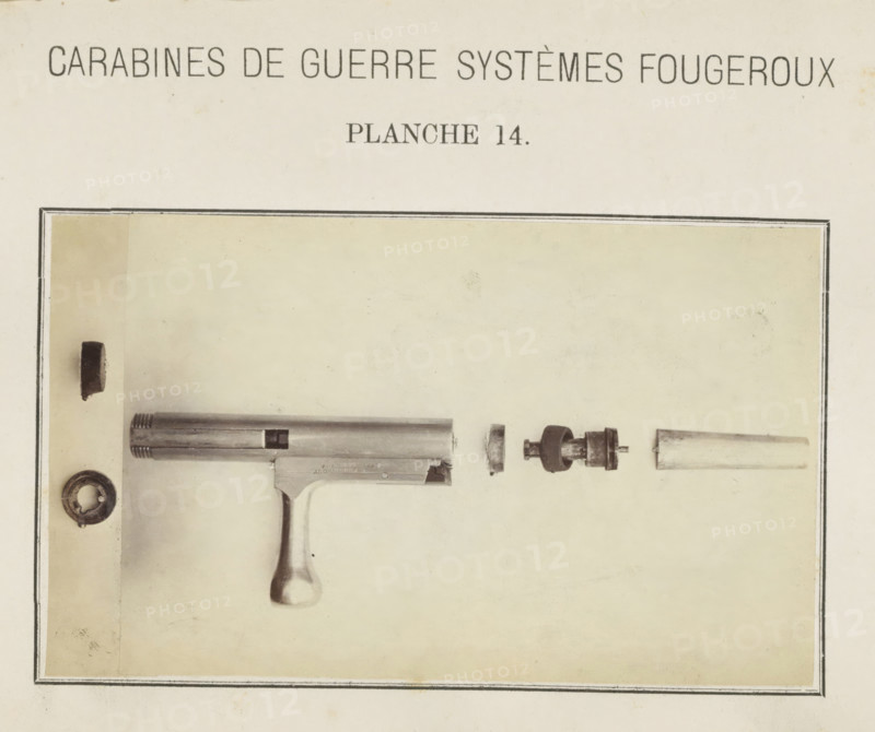 Safety catch of a rifle in parts, photograph, page, number: 'Planche 14.', inscription: 'Carabines de guerres systèmes Fougeroux', photographer: Edouard Magis, Liège, c. 1857 - in or before 1867, paper, albumen print, height 158 mm x width 96 mm, Image in section at the back., firearms: rifle, A faded sepia-toned page with a rectangular bordered area containing a partially visible metal firearm frame and a rounded grip, accompanied by several cylindrical and ring-shaped metal components arranged horizontally above and beside the frame, all set against a light, slightly mottled background.