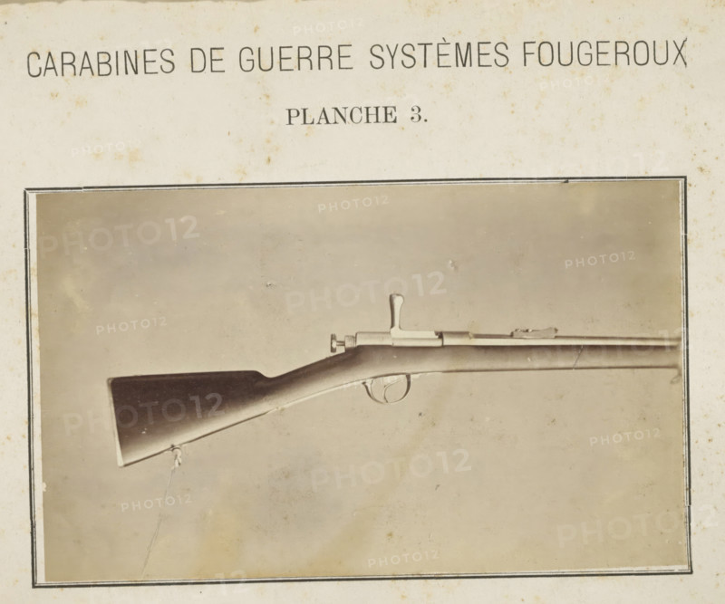 Butt of a rifle, photograph, page, inscription: 'Carabines de guerres systèmes Fougeroux', number: 'Planche 3.', photographer: Edouard Magis, Liège, c. 1857 - in or before 1867, paper, albumen print, height 159 mm x width 97 mm, Image in section at the back., firearms: rifle, A sepia-toned photograph of a rifle displayed horizontally within a dark rectangular border on aged paper, showing the wooden butt, curved stock, trigger guard, and metal bolt mechanism, with a sling attached near the butt and the barrel extending toward the right, all set against a plain, slightly mottled background.