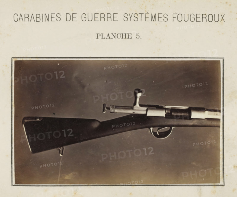 Butt of a rifle, photograph, page, number: 'Planche 5.', inscription: 'Carabines de guerres systèmes Fougeroux', photographer: Edouard Magis, Liège, c. 1857 - in or before 1867, paper, albumen print, height 158 mm x width 96 mm, Image in section at the back., firearms: rifle, A sepia-toned photograph shows the rear half of a rifle mounted horizontally inside a bordered frame on a light background; the wooden stock is dark with a smooth curved shoulder, a metal sling swivel attached near its end, a metal bolt handle and cylindrical bolt assembly with knurled adjustment knob, a trigger and curved trigger guard, and a contrasting lighter metal band near the muzzle area, all set against a plain darker backdrop within the photograph.