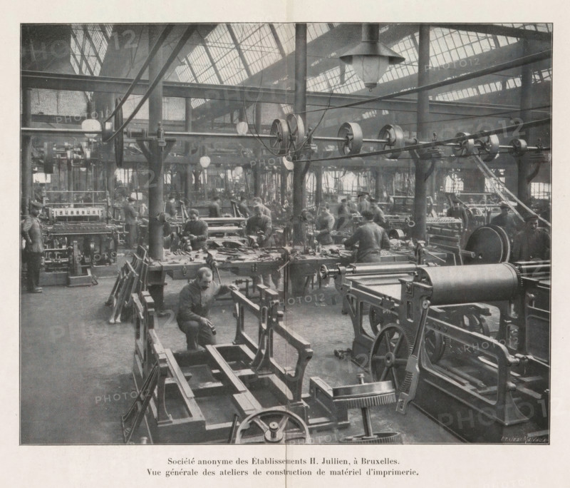 View of a workshop for the construction of printing equipment in the Société anonyme des Établissements H. Jullien in Brussels, Société anonyme des Établissements H. Jullien, à Bruxelles., Vue générale des ateliers de construction de material d'imprimerie, page, photomechanical print, Brussels, cliché maker: Jean Malvaux, c. 1906 - in or before 1911, Jean Malvaux, photographer, cliché maker, paper, autotypie, height 149 mm x width 188 mm, Print on second and third unnumbered page after page 176., tools, implements of printer, A large industrial interior with rows of machinery and workbenches filling the floor, overhead beams and pulleys stretching across the space, large windows in the roof letting light in, hanging lamps suspended from the ceiling, multiple workers at benches operating tools and machines, visible gears, wheels, belts, and mechanical frames, tall support columns rising through the workspace, scattered tools and parts on the benches, and a foreground view of machine fra...