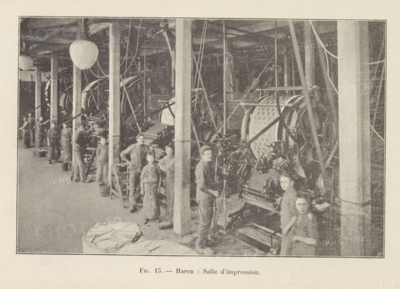 View of the interior of a printing shop in Haren, Belgium, page, photomechanical print, inscription: 'Fig. 15. - Haren: Salle d'impression.', monogram: 'AN', photographer: unknown, Haren (Brussels), cliché maker: Jean Malvaux, c. 1901 - in or before 1906, unknown, Jean Malvaux, photographer, cliché maker, Brussels, paper, autotype, height 170 mm x width 110 mm, printing, printing office, workshop-interior, paper (writing material), A wide interior scene shows a long room with tall vertical posts and beams stretching from foreground to background, overhead lighting globes hanging from the ceiling, numerous large mechanical machines with visible gears and belts aligned along the length of the room, many cables and rods suspended and connected to the machinery, groups of people standing and working beside the machines wearing plain, dark clothing and aprons, a few young individuals positioned near the front looking toward the viewer, stacks of folded material on the floor in the foregroun...
