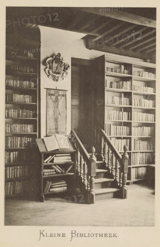 Interior of the library of Christoffel Plantijn, Small library, page, photomechanical print, maker: Joseph Maes, c. 1881 - in or before 1886, paper, collotype, photoprint, height 160 mm x width 110 mm, Print on second unnumbered page after page 136., study, 'studiolo', library, A monochrome photograph of an interior showing wooden bookshelves filled with books on both sides of a short carved staircase with turned balusters and newel posts; a small lectern or bookstand beside the staircase holds an open large book and has additional books on its lower shelves; a narrow vertical hanging image is mounted on the wall above the lectern and an ornamental crest is displayed above it; exposed ceiling beams run across the top of the room and a dark doorway is visible behind the staircase.