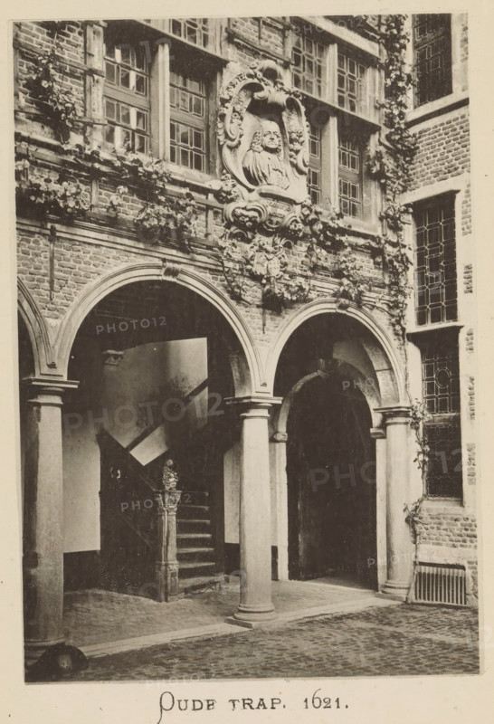 Courtyard with stairs of the house of Christoffel Plantijn, Old stairs 1621, page, photomechanical print, maker: Joseph Maes, c. 1881 - in or before 1886, paper, collotype, photoprint, height 160 mm x width 110 mm, Print on second unnumbered page after page 112., courtyard, staircase, A sepia-toned photograph of a brick courtyard façade showing arched openings supported by round columns, a staircase with a carved newel post, decorative stone reliefs above the arches including a framed sculpted bust set into ornate scrollwork, rectangular leaded windows with multiple panes, climbing vines along the brickwork, a cobbled ground surface, and a portion of a metal grate set into the wall.