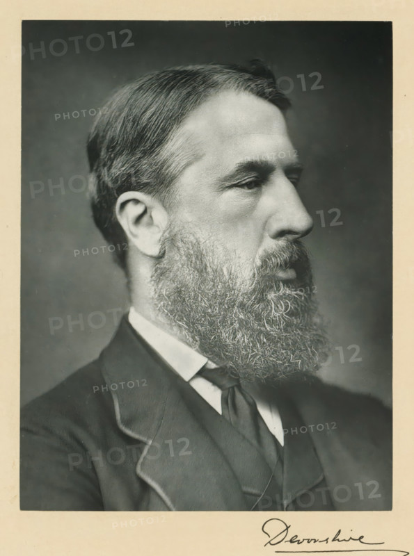 His grace the duke of Devonshire, photograph, page, annotation, inscription: '25 Old Bond St. London, W.', photographer: Bassano & Co., London, c. 1893 - c. 1903, paper, carbon print, height 226 mm x width 171 mm, Photo on frontispiece., historical persons (portraits and scenes from the life) ((full) bust portrait), A black and white portrait of a man in profile facing right showing short combed hair, a full beard and mustache, a visible ear, a high forehead, and a solemn facial expression; he is wearing a dark suit jacket with a visible lapel, a high white shirt collar, and a dark necktie, all framed by a light border around the photograph.