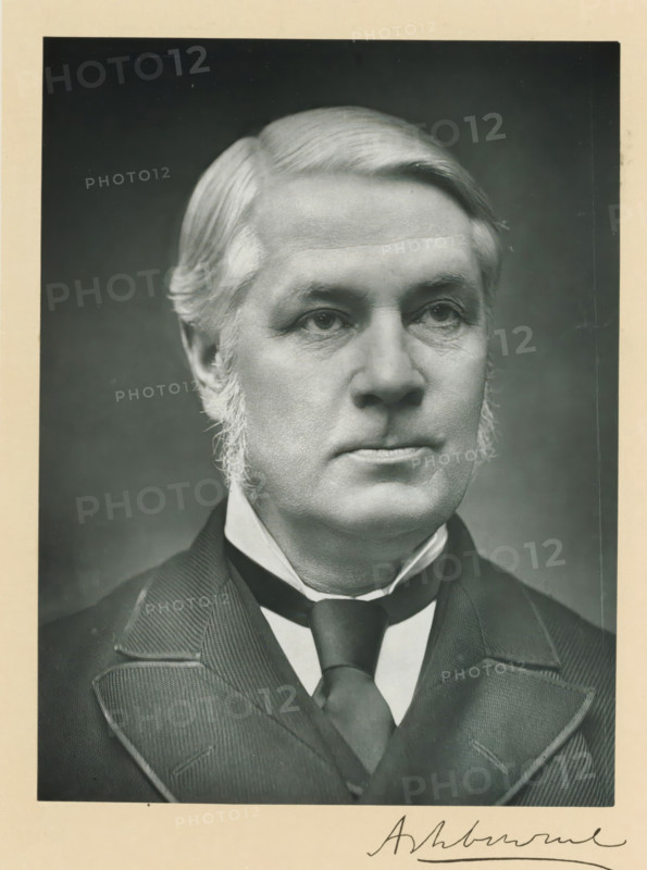 The right honorable lord Ashbourne, photograph, page, inscription: '17, Baker St, London, W.', annotation, photographer: Russell & Sons, c. 1893 - c. 1903, paper, carbon print, height 228 mm x width 171 mm, Person, Lord Edward Gibson, historical persons (portraits and scenes from the life) ((full) bust portrait), A black and white portrait of a middle-aged man shown from the shoulders up wearing a dark suit jacket with wide lapels, a high-collared shirt, and a dark tie; he has neatly combed light hair with sideburns, a smooth forehead, and a neutral facial expression with visible wrinkles around the eyes and mouth, set against a plain dark background and bordered by a light-colored mat.