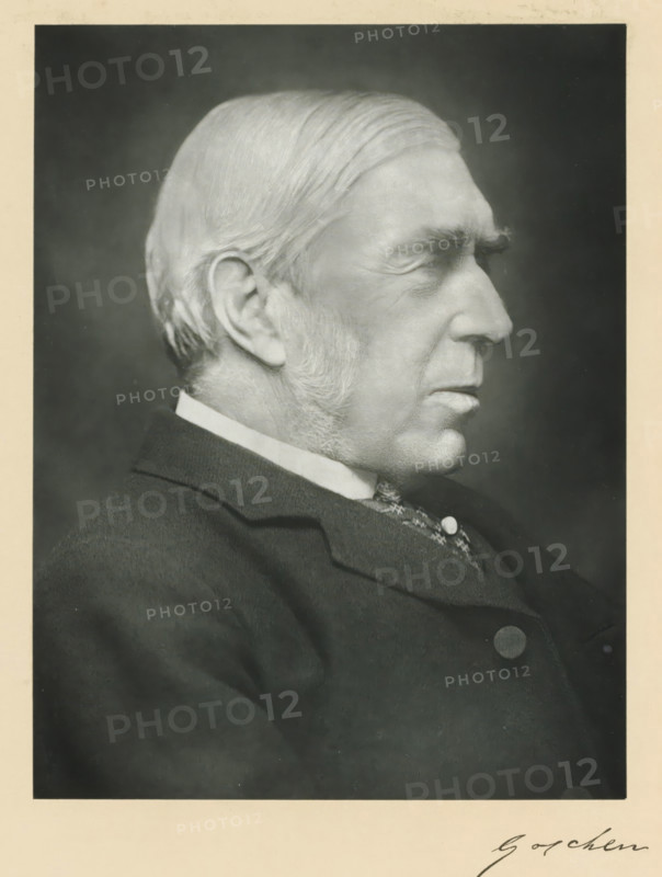 The right honorable Viscount Goschen, photograph, page, annotation, inscription: '17, Baker St, London, W.', photographer: Elliott & Fry, c. 1893 - c. 1903, paper, carbon print, height 227 mm x width 171 mm, Person, George Goschen, historical persons (portraits and scenes from the life) ((full) bust portrait), A black and white portrait of an older man in profile facing right, showing a close-up of his head and upper torso; he has neatly combed hair swept back, prominent sideburns, a high forehead with visible wrinkles, a pronounced nose, and a closed mouth with a firm expression; he is wearing a dark suit jacket with a visible collar and a patterned vest underneath, with a round button on the jacket; the background is plain and dark, and the image has a light border surrounding it.