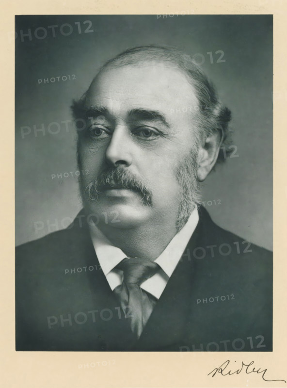 The right honorable Viscount Ridley, photograph, page, inscription: 'Newcastle-on-Tyne', annotation, photographer: Ruddock, London, c. 1893 - c. 1903, paper, carbon print, height 227 mm x width 171 mm, Person, Matthew White Ridley, historical persons (portraits and scenes from the life) ((full) bust portrait), A black-and-white portrait of a middle-aged man shown from the shoulders up, facing slightly to the viewer's left, with a high forehead and receding hairline, full sideburns and a thick moustache, wearing a dark jacket and a white shirt with a loosely knotted necktie, set against a plain, softly shaded background and framed by a light border.