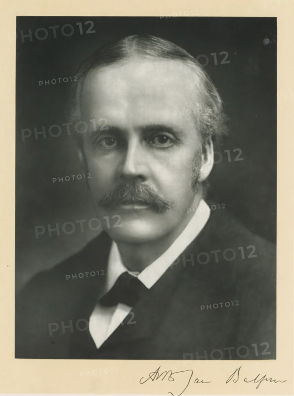 The right honorable Arthur James Balfour, photograph, page, inscription: '55, Baker St, London, W.', annotation, photographer: Elliott & Fry, c. 1893 - c. 1903, paper, carbon print, height 227 mm x width 171 mm, Person, Arthur James Balfour, historical persons (portraits and scenes from the life) ((full) bust portrait), A black and white portrait of a middle-aged man shown from the chest up, with a high forehead and neatly combed hair, a full mustache, sideburns, and a composed expression, wearing a dark coat over a white shirt and a dark bow tie, set against a dark background and surrounded by a light-colored border.