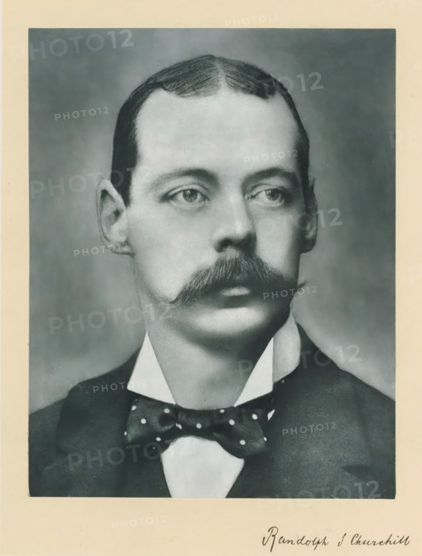 The right honorable the late lord Randolph Spencer Churchill, photograph, page, annotation, inscription: 'Rue d'Anjou, 51, Paris.', photographer: Félix Nadar, Paris, c. 1890 - c. 1895, Félix Nadar, photographer, paper, carbon print, height 229 mm x width 171 mm, Person, Lord Randolph Churchill, historical persons (portraits and scenes from the life) ((full) bust portrait), A black-and-white portrait of a man from the shoulders up showing a neatly combed hairstyle with a center part, a prominent curled mustache, light-colored eyes looking slightly to the side, and a high-collared shirt with a dark jacket and a polka-dotted bow tie.