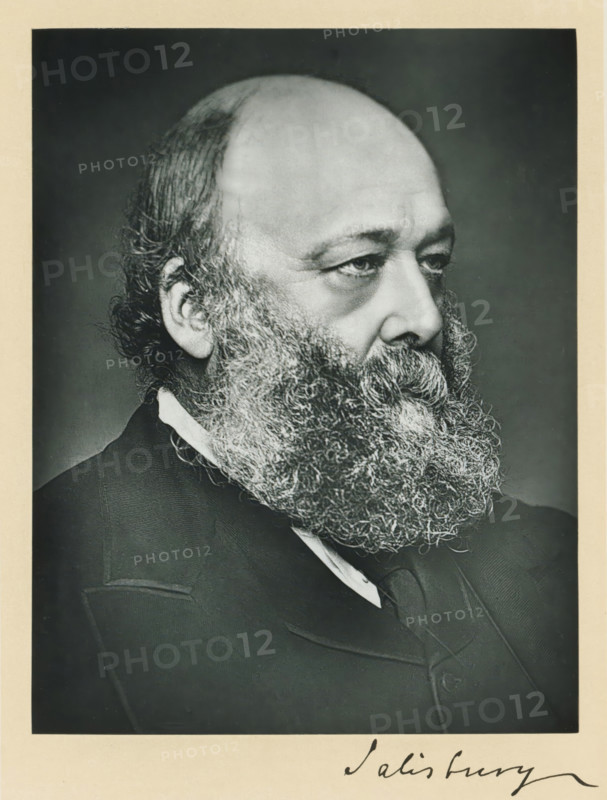 The most noble the marquis of Salisbury, KG, photograph, page, annotation, inscription: '17, Baker St, London, W.', photographer: Russell & Sons, c. 1893 - c. 1903, paper, carbon print, height 227 mm x width 171 mm, Photo on frontispiece., Person, Robert Gascoyne-Cecil (Marquis of Salisbury), historical persons (portraits and scenes from the life) ((full) bust portrait), A black and white portrait of an older man shown in profile from the shoulders up, featuring a high forehead, receding hair at the crown, and thick curly hair at the sides and back of his head; he has a full, dense beard with tight curls that covers his chin and neck, prominent eyebrows, and a thoughtful expression in his eyes; he wears a dark suit jacket with a visible lapel, a white shirt collar, and a dark tie, all set against a plain dark background and surrounded by a light border.