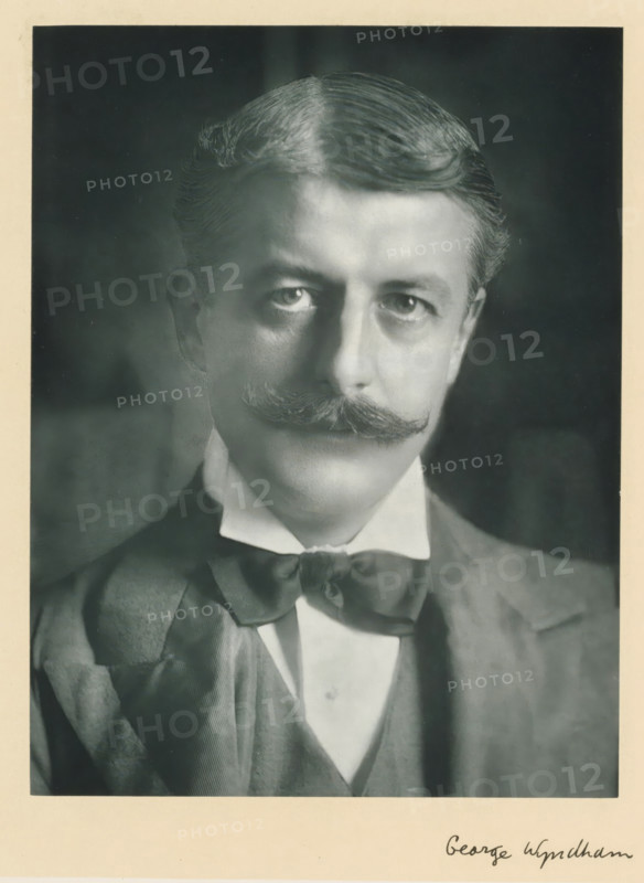 The right honorable George Wyndham, photograph, page, annotation, inscription: '55, Baker St, London, W.', photographer: Elliott & Fry, c. 1893 - c. 1903, paper, carbon print, height 227 mm x width 171 mm, Person, George Wyndham (4th Duke of Egremont), historical persons (portraits and scenes from the life) ((full) bust portrait), A black-and-white portrait of a man from the chest up wearing a suit jacket, waistcoat, high-collared shirt, and a bow tied at the neck; he has neatly combed hair with a side part and a prominent curled mustache, with a neutral facial expression and direct gaze toward the camera, set against a dark, softly textured background and framed by a light border.