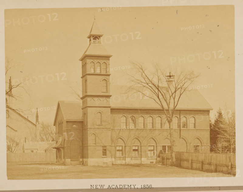 New Academy. 1856, View of the second location of the Friends Academy in New Bedford, Massachusetts, photograph, page, c. 1871 - in or before 1876, photographer, paper, albumen print, height 108 mm x width 145 mm, scholastic education, tuition, civic architecture, edifices, dwellings, North America, New Bedford, A sepia-toned photograph of a multi-story brick building with a tall square tower topped by a steep pyramidal roof and an open belfry, a row of arched windows along the upper floor, and arched entryways on the ground level; leafless trees stand in front of the building, a wooden fence runs along the right side, and a small pitched-roof annex projects from the left side of the main structure.