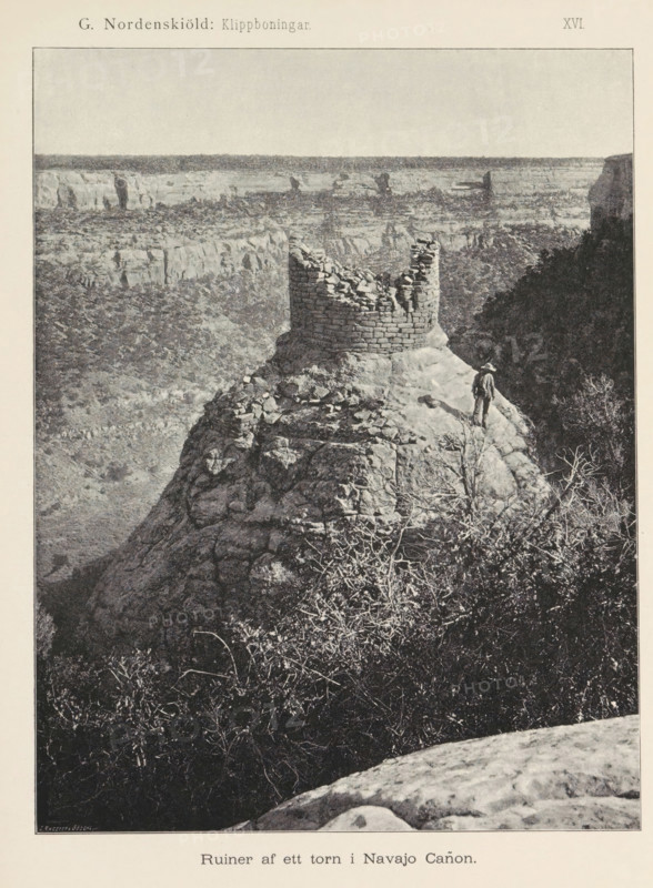 Ruin på mesan, View of the ruin, probably in Mesa Verde National Park, page, photomechanical print, number: 'Fig. 44.', name, photographer: Gustaf Nordenskiöld (possibly), Mesa Verde National Park, cliché maker: Angerer & Göschl, C., Vienna, c. 1891 - in or before 1893, clichémaker, North America, Lower Austria, Colorado, paper, autotypie, height 87 mm x width 148 mm, ruin of a dwelling, house, castle, A grayscale photograph of a rocky canyon scene showing a cylindrical stone ruin perched on a rounded rock outcrop near the edge of a cliff, with sections of the ruin missing and scattered stones around its base; a lone figure wearing a hat stands on the rock near the ruin looking outward; steep canyon walls and layered rock formations extend into the background beneath a wide pale sky, while sparse vegetation and leafless branches are visible on the slopes and in the foreground.