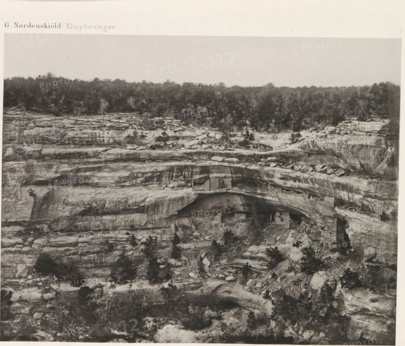 View of a cliff dwelling, Kodak House, in Mesa Verde National Park, The Kodak House, page, photomechanical print, number: 'I', inscription: 'G. Nordenskiöld: Klippboningar.', photographer: Gustaf Nordenskiöld, Mesa Verde National Park, cliché maker: Librairies-Imprimeries Réunies (Ancienne Maison Quantin), Paris, c. 1891 - in or before 1893, North America, Colorado, paper, photoaquatint, height 187 mm x width 240 mm, ruin of a dwelling, house, castle, A wide grayscale photograph showing layered rock formations with horizontal striations and ledges, sparse vegetation growing on and between the rocks, a tree line along the top edge, uneven rocky surfaces with cracks and boulders, an overhanging rock shelf creating a shallow recess, and lighter sky above the distant treeline.