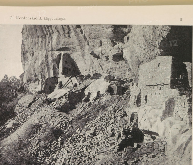 View of Long House in Mesa Verde National Park, Long House i Navajo Cañon (…), page, photomechanical print, name, number: 'Fig. 10.', photographer: Gustaf Nordenskiöld (possibly), Mesa Verde National Park, cliché maker: Angerer & Göschl, C., Vienna, c. 1891 - in or before 1893, clichémaker, North America, Lower Austria, Colorado, paper, autotypie, height 90 mm x width 147 mm, ruin of a dwelling, house, castle, cave-dwelling, A grayscale photograph showing a rocky cliff face with layered stone formations and ledges, with stone ruins built into and along the cliff including stacked masonry walls and rectangular openings, rubble and loose rocks scattered on a sloped foreground, a few shrubs and small trees near the base, and a dark recessed area within the cliff on the right side.