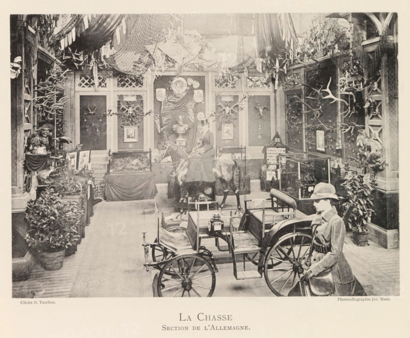 Exhibition of German hunting objects during the world exhibition in Antwerp, La Chasse Section de l'Allemagne, page, photomechanical print, photographer: Th. Lantin, Antwerp, cliché maker: Joseph Maes, 1894, Th. Lantin, Joseph Maes, photographer, cliché maker, paper, collotype, photoprint, height 160 mm x width 219 mm, spoils of the hunt, game, venison, hunting, chase, world fair, world exhibition, exhibition, show, A large indoor scene shows a room filled with mounted animal trophies and hunting paraphernalia arranged along paneled walls, with numerous antlers and skulls displayed on mounts and plaques, leafy plants in pots lining the floor, and nets and fabric draped from the ceiling; a mannequin dressed in riding attire stands beside a horse and cart positioned in the foreground, while framed pictures, a bust on a pedestal, glass display cases, and various small objects occupy tables and shelves throughout the space.