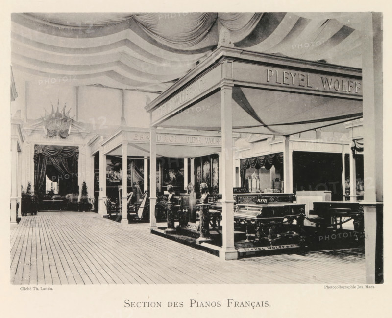 Section des Pianos Français, Exhibition of French pianos during the World Exhibition in Antwerp, page, photomechanical print, photographer: Th. Lantin, Antwerp, cliché maker: Joseph Maes, 1894, paper, collotype, light printing, height 160 mm x width 219 mm, grand piano, world fair, world exhibition, exhibition, show, An indoor exhibition space with a striped fabric ceiling draped in sweeping curves and a wooden plank floor; a series of columned booths and canopies occupy the area, each sheltering furniture and musical instruments including ornate pianos and carved statues; heavy curtains and decorative pediments frame openings at the back, and framed paintings hang on the inner walls of some booths; the scene shows a mix of dark and light tones with shadows cast by the canopy structures and various ornamental details on the furnishings.