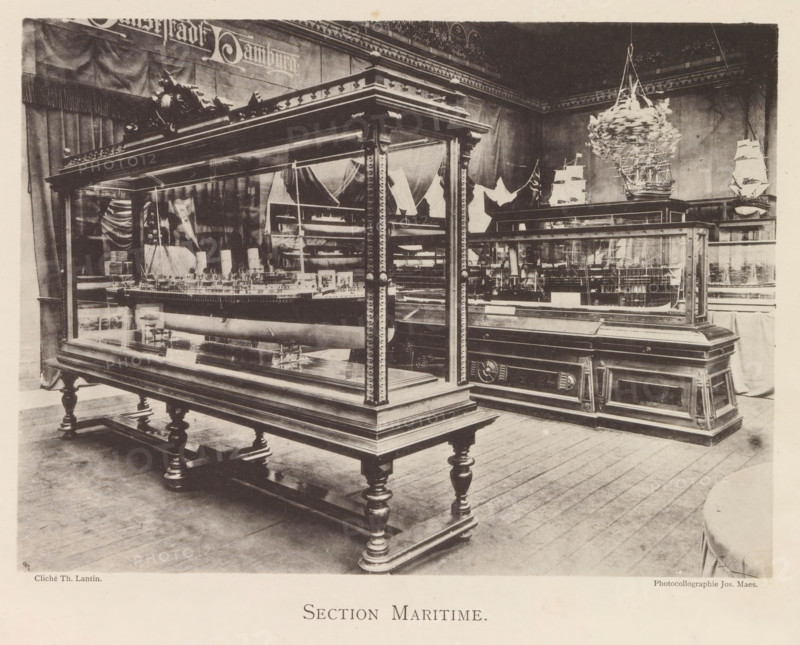 Exhibition of ship models during the World Exhibition in Antwerp, Section Maritime, page, photomechanical print, photographer: Th. Lantin, Antwerp, clichémaker: Joseph Maes, 1894, paper, collotype, photoprint, height 160 mm x width 218 mm, ship-model, world fair, world exhibition, exhibition, show, A room filled with large wooden display cases with glass sides and ornate carved legs and trim, each case containing detailed ship models visible through the glass; a suspended miniature ship hanging from the ceiling; draped fabric and flags on the walls behind the cases; wooden floorboards beneath the display furniture.