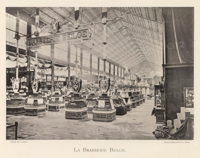 Exhibition of Belgian foodstuffs during the World Exhibition in Antwerp, La Brassie Belge, page, photomechanical print, photographer: Th. Lantin, Antwerp, clichémaker: Joseph Maes, 1894, paper, collotype, photogravure, height 155 mm x width 218 mm, industries, food, drink, stimulants, world fair, world exhibition, exhibition, show, A large indoor exhibition hall with a high vaulted roof supported by tall iron columns and trusses, rows of display tables and pedestals arranged beneath the roof, ornate hanging shields and decorative emblems suspended above several displays, numerous stacked bottles and packaged products arranged in pyramidal formations on labeled bases, draped fabric and garlands along the upper walls and between columns, a wooden plank floor extending toward the foreground, a curtained partition and covered objects to the right, and large paned windows along the left wall letting light into the space.