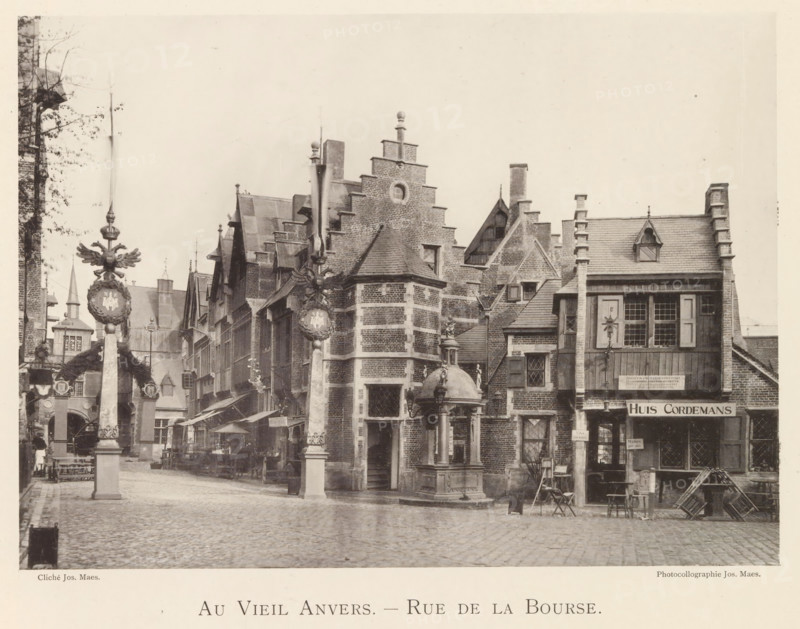 Beursstraat in Antwerp, Au vieil Anvers - Rue de la Bourse, page, photomechanical print, photographer: Th. Lantin, Antwerp, printer (person): Joseph Maes, c. 1890 - in or before 1894, printer (person), paper, collotype, photoprint, height 158 mm x width 220 mm, street, facade (of house or building), A cobblestone street lined with tall brick buildings featuring stepped gables, dormer windows, and chimneys, with a square stone fountain topped by a small domed canopy and a statue in the center foreground, decorative stone pillars topped with ornamental crests and winged figures standing along the street, awnings and market stalls with tables and chairs set beneath them, wooden shutters and paned windows on the building facades, a small wooden balcony and a storefront with an overhanging roof, stacked wooden crates and a folding chair near the right side, and a narrow alleyway and arch visible between the buildings on the left.