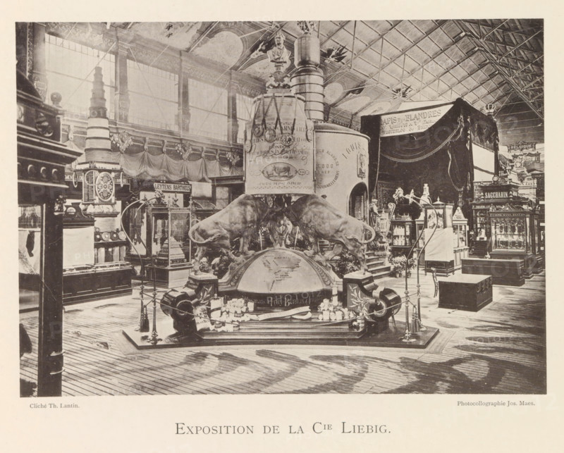 Exhibition of Liebig Meat Extracts during the World Exhibition in Antwerp, Exposition de la Cie Liebig, page, photomechanical print, photographer: Th. Lantin, Antwerp, clichémaker: Joseph Maes, 1894, paper, collotype, photogravure, height 144 mm x width 204 mm, foodstuffs, still life of foodstuffs, world fair, world exhibition, exhibition, show, A large indoor exhibition space with a high vaulted ceiling and tall windows shows an ornate central display featuring two large sculpted bulls positioned on a rounded base in front of a tall cylindrical column with decorative bands and medallions, topped by a bust. Surrounding the central piece are display cabinets, pedestals, and ornate stands holding smaller objects and models, with draped fabric and tasselled curtains hanging in parts of the background. The floor is wooden planks with visible grain and a pattern of light and shadow, and various stands, ropes, and decorative posts form a perimeter around the main exhibit. Additional cabinets...