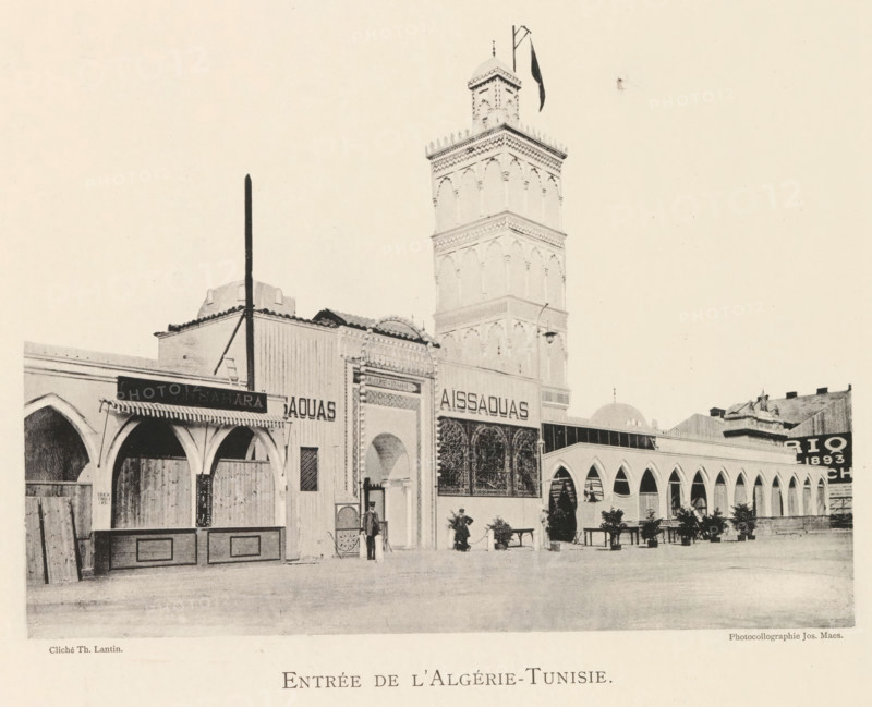 Entrée de l'Algérie-Tunisie, Exterior of the pavilion of Algeria and Tunisia at the world exhibition in Antwerp, page, photomechanical print, photographer: Th. Lantin, Antwerp, printer (person): Joseph Maes, 1894, Th. Lantin, Joseph Maes, photographer, printer (person), paper, collotype, photoprint, height 161 mm x width 219 mm, facade (of house or building), world fair, world exhibition, A sepia-toned street scene shows a row of connected buildings with arched openings and decorative facades, including a tall ornate tower with layered sections and a small dome at the top, a flagpole and a flag near the tower peak, awnings and shutters over some arches, wrought-iron or lattice panels in front of one entrance, potted plants and benches along the building front, a few people standing or walking near the entrances, a vertical pole supported by diagonal stays in front of one building, and varied rooflines and architectural details across the structures.