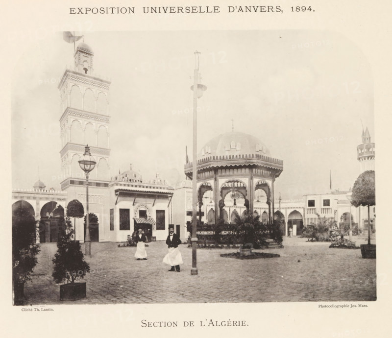 Exterior of the Algeria pavilion at the World Exhibition in Antwerp, Section de l'Algérie, page, photomechanical print, photographer: Th. Lantin, Antwerp, printer (person): Joseph Maes, 1894, Th. Lantin, Joseph Maes, photographer, printer (person), paper, collotype, photoprint, height 163 mm x width 219 mm, facade (of house or building), world fair, world exhibition, A sepia-toned scene shows an open courtyard with ornate pavilion structures and a tall intricately detailed tower, arched colonnades along the background, decorative domes and a small turreted tower at one side, a central octagonal kiosk with scalloped arches and a domed roof, a tall lamp post and another pole rising near the kiosk, potted trees and plants arranged around the paved ground, two men wearing dark jackets and long white aprons walking in the foreground, and various architectural details such as carved cornices, window openings, and ornamental railings visible on the buildings.