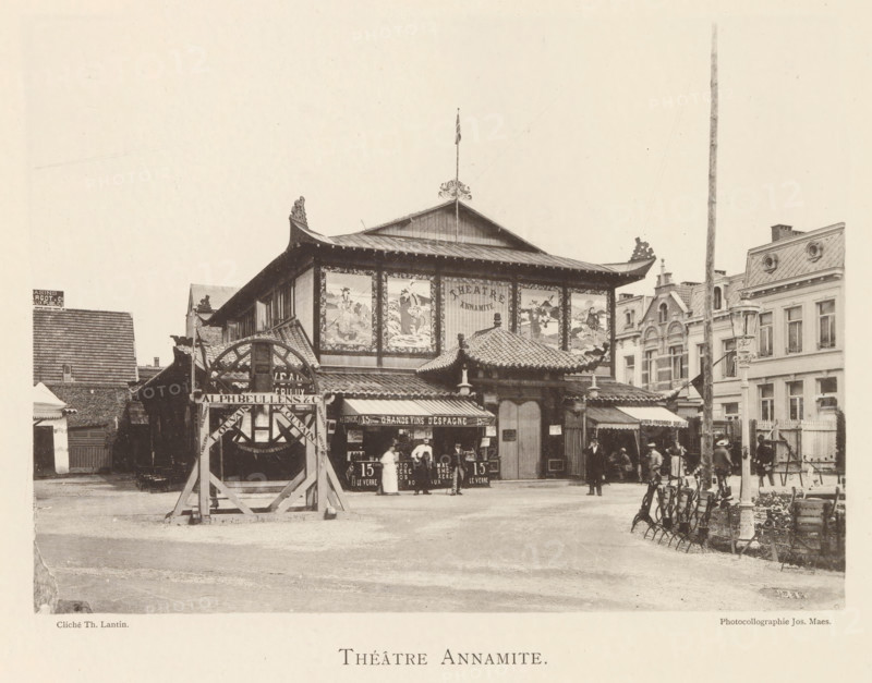Annamite Theatre, Exterior of the Annamite Theatre at the World Exhibition in Antwerp, page, photomechanical print, photographer: Th. Lantin, Antwerp, printer (person): Joseph Maes, 1894, printer (person), paper, collotype, photogravure, height 161 mm x width 220 mm, façade (of house or building), theatre (building), world fair, world exhibition, A wide street scene centered on a two-story building with a pagoda-style roof featuring ornate upturned eaves and decorative roof tiles, a central entrance with a tiled canopy and carved finials, and large framed panels on the upper façade displaying painted scenes; people stand and walk in front of the building near market stalls and kiosks that have awnings and displayed goods, while to the left a timber structure with a circular wheel-like element stands on a wooden frame; surrounding buildings of varying European architectural styles border the scene with mansard roofs and ornate window surrounds, and a tall slender pole rises near the rig...