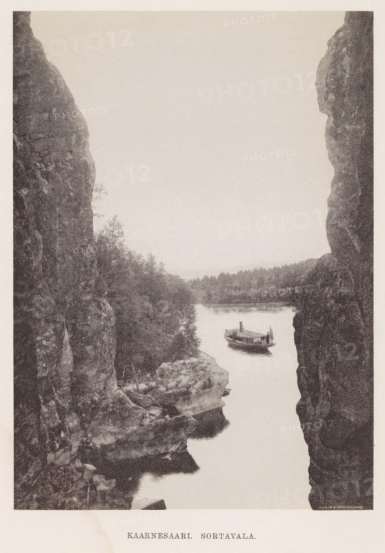 View of a steamboat launching from a spot between two rocks, Kaarnesaari. Sortavala, page, photomechanical print, photographer: Impi Backman, cliché maker: anonymous, printer (person): Weilin & Göös, c. 1888 - c. 1893, printer (person), paper, autotypie, height 224 mm x width 163 mm, trees, landscapes with waters, waterscapes, seascapes (in the temperate zone), steamship, motorship, rocks, Karelia, A narrow vertical view framed by tall rocky cliffs on either side reveals a calm river flowing between them with a small wooden boat floating near the center of the water, the boat showing a covered cabin and a single flag at its stern; dense treeline and low wooded hills line the far riverbank, and textured rock shelves and vegetation appear along the near cliff edges, all rendered in a monochrome, grainy photographic tone.