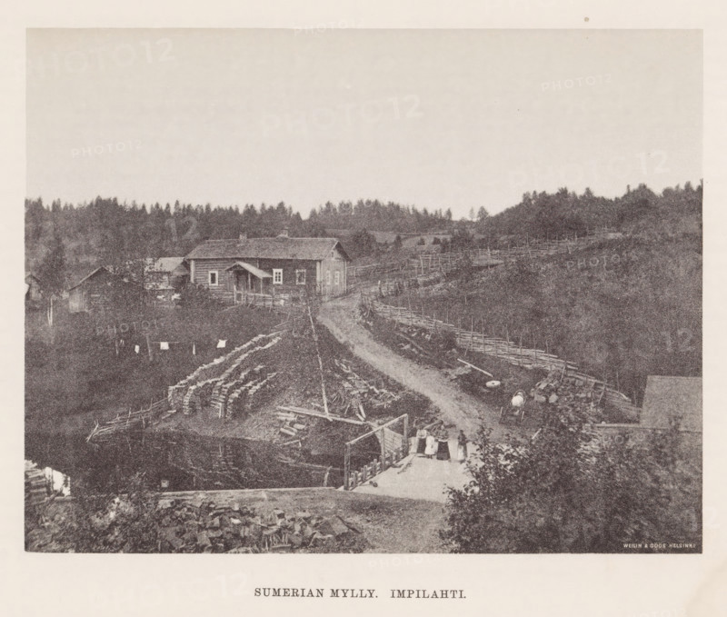 View of a path through a hilly landscape with houses, Sumerian mylly. Impilahti, page, photomechanical print, photographer: Impi Backman, cliché maker: anonymous, printer (person): Weilin & Göös, c. 1888 - c. 1893, printer (person), paper, autotypie, height 161 mm x width 210 mm, road, path, bridge, (high) hill, civic architecture, edifices, dwellings, Karelia, A grainy black-and-white photograph of a rural scene showing a dirt road curving through a fenced landscape toward a cluster of wooden buildings, including a house with a pitched roof and a small covered porch, surrounded by fences and stacks of cut logs; in the foreground there is a wooden walkway or platform with several figures standing on it and laundry hanging nearby, a body of water reflecting parts of the scene, and scattered farm implements and barrels; the background features a tree line of coniferous trees and gently rolling hills under a pale sky.
