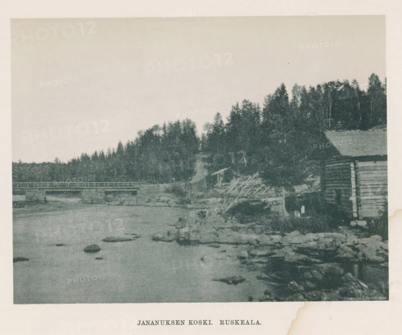 Jananuksen koski - Ruskeala, View of a river in Ruskeala, page, photomechanical print, photographer: Impi Backman, cliché maker: anonymous, printer (person): Weilin & Göös, c. 1888 - c. 1893, printer (person), paper, autotypie, height 157 mm x width 206 mm, river, bridge, civic architecture, edifices, dwellings, Karelia, A grainy landscape image showing a body of water in the foreground with scattered rocks and a shoreline, a wooden bridge crossing the water toward the left, a hillside covered with dense trees and foliage along the right and center, and a rustic wooden structure partially visible on the right edge.