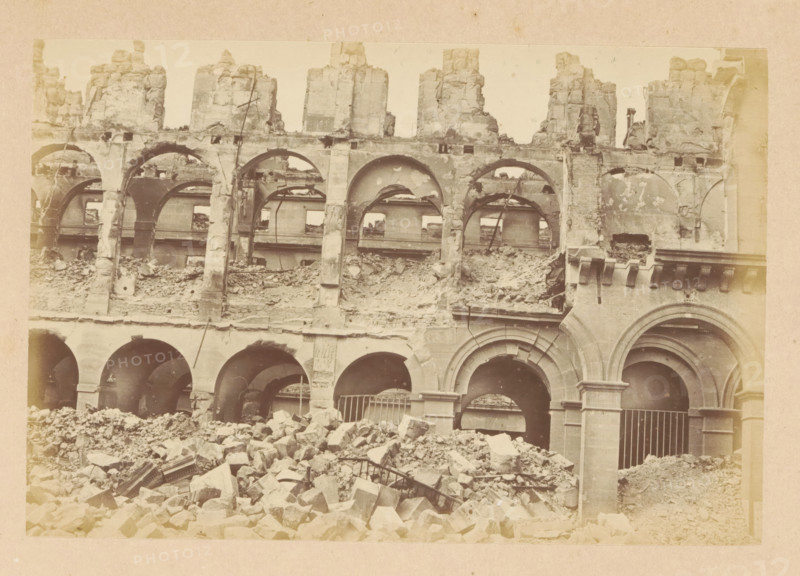 Ministère des finances, View of a destroyed Ministry of Finance, photograph, page, 1871, photographer, paper, albumen print, albumendruk, height 101 mm x width 151 mm, ruin of a dwelling, house, castle, palace, Paris, A large stone building facade with multiple rounded arches and upper-level arched openings, many of the stones chipped and crumbling, a pile of rubble and broken masonry in front of the arches, exposed structural elements and partial interior walls visible through the openings, vertical supports and carved stone details around some arches, and a generally worn and damaged surface across the visible sections.