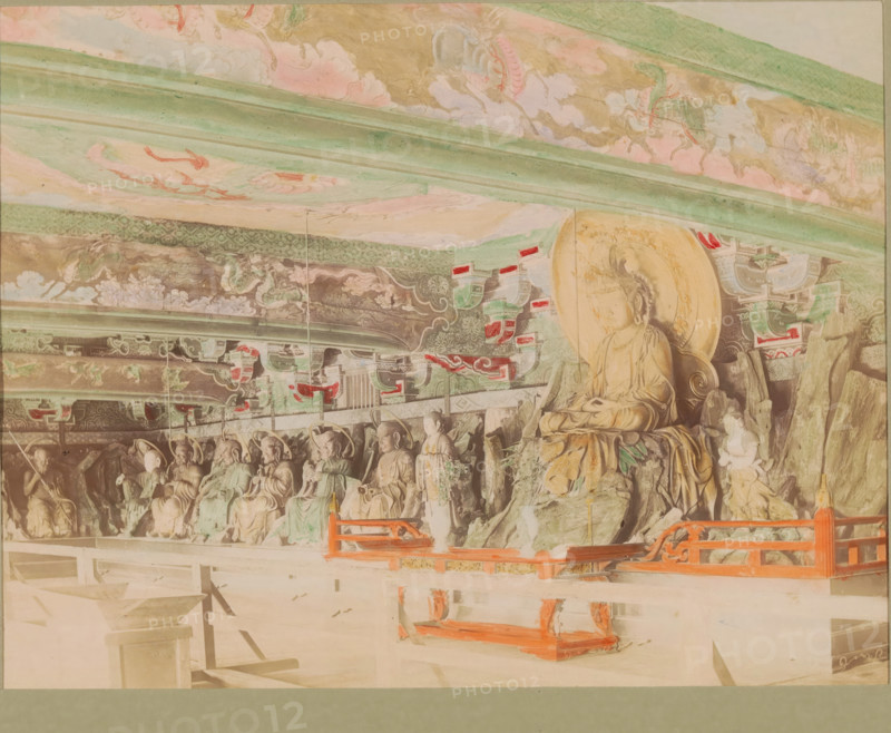 Sculptures in the Chion-in temple in Kyoto, photograph, page, Chion-in, Japan, c. 1887 - in or before 1897, photographer, colorer (graphic design artist), Kinki, Kyoto, paper, albumen print, hand coloring, photographie peinte, height 186 mm x width 243 mm, Photo for page 179., sculpture, temple, shrine, Hinduism, Buddhism, Jainism, Buddha, founder of Buddhism, interior, representation of a building, A row of carved stone figures seated against a decorated wall, with a larger seated figure on a raised rock formation at the right, all beneath an ornate painted ceiling with flowing cloud and dragon motifs in muted greens, pinks, and golds, with patterned horizontal beams and decorative brackets featuring red and green accents, and a low wooden railing painted bright red in front of the figures.