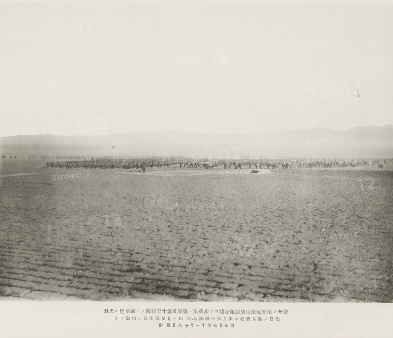 Requisition of the Japanese army south of Chinchow, Advance of the first, and portion of the fifteenth, infantry regiments after their sudden muster at Sooheatun, S. of Kinchow, page, photomechanical print, inscription: 'The fall of Kinchow.', inscription: 'The horseman at the head of the army is the Commander of the First Regiment. The mountains in the distance are situated on the N. of Kinchow Bay.', photographer: Ordnance Survey, China, cliché maker: Kazumasa Ogawa, Japan, 1894-11-18, paper, collotype, photoprint, height 211 mm x width 278 mm, army 'en route', A wide, flat landscape with a textured, ridged foreground that transitions to a distant, low horizon where a long, horizontal line of people and animals is assembled, appearing as small, dark figures against a pale sky and a faint silhouette of hills in the background.