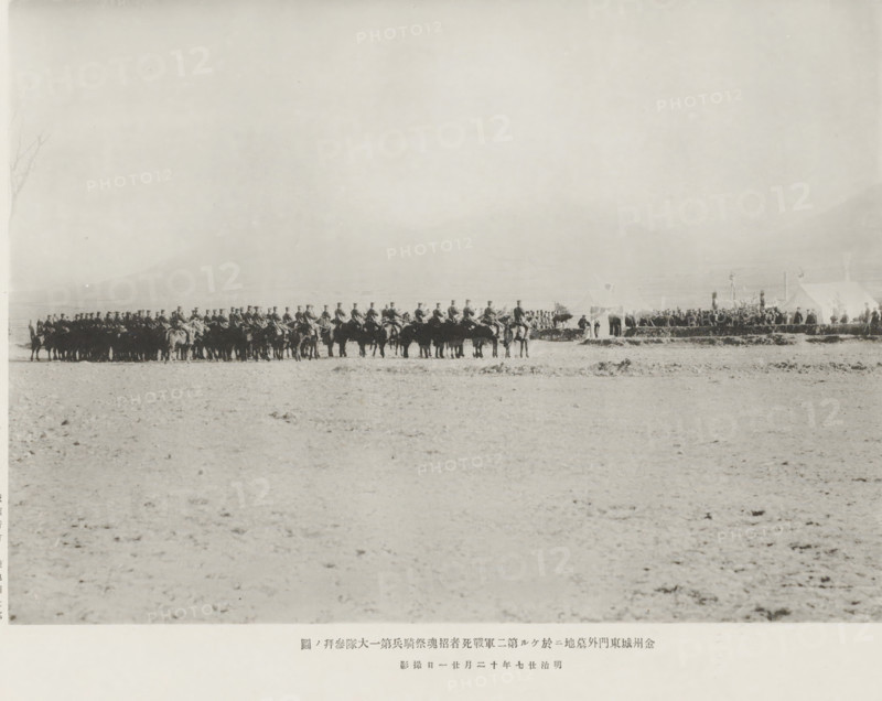 A service hero in memory of those fallen in the second army, at the cemetery outside the east gate of Kinchow: the salute of the first cavalry battalion, page, photomechanical print, inscription: 'The fall of Kinchow.', photographer: Ordnance Survey, China, cliché maker: Kazumasa Ogawa, Japan, 1894-11-21, paper, collotype, photoprint, height 203 mm x width 284 mm, horse, funerary ceremonial, military salutes, A wide, pale landscape fills the image with a low horizon line, and near that horizon a long line of mounted figures forms a dark silhouette across the scene, each person seated on a horse and wearing a uniform with high headgear; to the right of the mounted line there are a few tents and groups of standing people gathered around them, with some upright poles or standards nearby, while the foreground shows a flat, textured ground with scattered small clumps and rough patches.