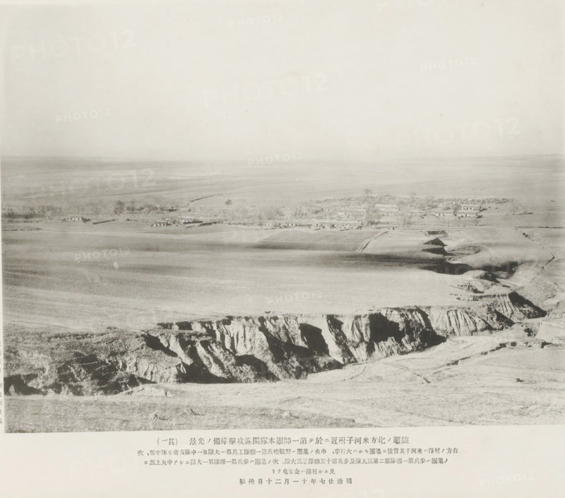 Preparations for advance and attack being made by the main body of the first division near Mehotse, N. of Port Arthur, page, photomechanical print, inscription: 'The village to the right is Mehotse, The village seen higher up in the center is Kinheatun.', inscription: 'The fall of Port Arthur.', photographer: Ordnance Survey, Manchuria, cliché maker: Kazumasa Ogawa, Japan, 1894-11-20, paper, collotype, photoprint, height 201 mm x width 265 mm, city-view in general, 'veduta', A wide, pale landscape photograph showing a flat plain stretching to the horizon with a small cluster of low buildings and trees near the middle ground, lighter fields and furrows in front of them, and a rugged cliff edge with deep vertical rock faces in the foreground.