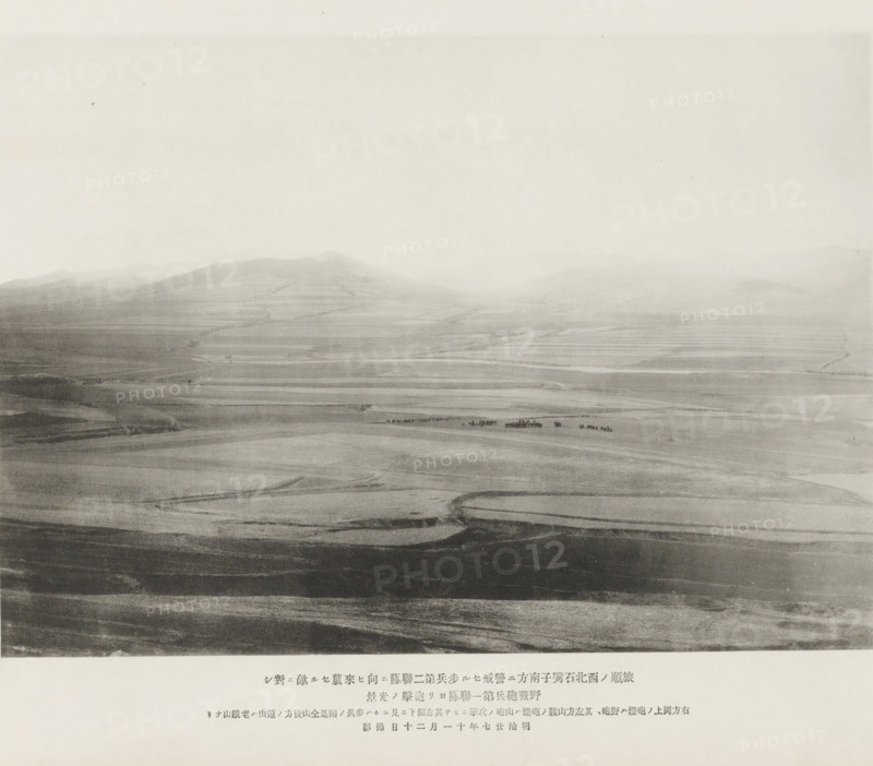 Cannonade of the first shield artillery regiment upon the Chinese advancing to attack the second infantry regiment stationed on the S. of Shihtsuytse, NW of Port Arthur, page, photomechanical print, inscription: 'The smoke on the hill on the right, The mountain in the distance is Laoteeshan.', inscription: 'The fall of Port Arthur.', photographer: Ordnance Survey, Manchuria, cliché maker: Kazumasa Ogawa, Japan, 1894-11-20, paper, collotype, photoprint, height 195 mm x width 277 mm, firearms: cannon, army 'en route', A wide, hazy landscape view with gently rolling hills and terraces fading into a pale sky, showing layered bands of darker and lighter ground across the foreground and midground, faint winding paths or tracks cutting through the fields, a small cluster of dark shapes near the center that appear distinct against the lighter terrain, and a broad expanse of open land stretching toward distant, softly outlined hills under a bright, featureless sky.