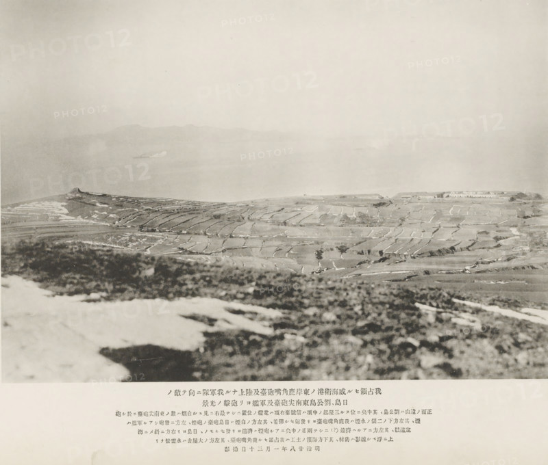 Attack made by the forts at Jih island and the south-eastern head of Liukung island and the Chinese men-of-war upon the already captured Lukeutsuy forts on the E. coast of Wei-Hai-Wei, and the Japanese army on land, page, photomechanical print, inscription: 'The mountain seen in the distance is Liukung Island, on its left is the torpedo station.', number: 'No. 19.', photographer: Ordnance Survey, Shandong, cliché maker: Kazumasa Ogawa, Japan, 1895-01-30, paper, collotype, photoprint, height 198 mm x width 284 mm, fortress, (military) attack, A wide, pale landscape photograph showing terraced fields on rolling hills in the foreground and middle distance, with faint variations in tone marking paths and boundaries between plots, and a distant body of water beyond the fields where a low, hazy ridge of land is visible on the horizon; the foreground contains out-of-focus darker ground and lighter patches that appear textured, while the sky above is light and largely uniform.