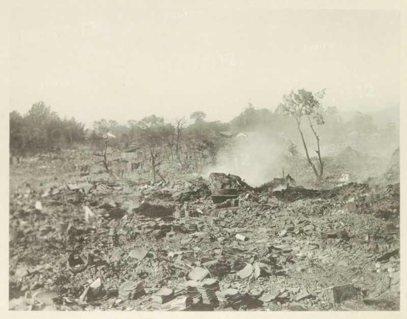 Destroyed buildings in Kasamatsu after an earthquake, page, photomechanical print, Kasamatsu, cliché maker: Kazumasa Ogawa, Japan, after 1891-10-28 - in or before 1892, photographer, Chubu, Gifu, paper, collotype, photoprint, height 216 mm x width 281 mm, ruin of a building, architecture, consequences of an earthquake, Mino–Owari earthquake 1891, A wide, sepia-toned scene of rubble and debris stretching toward a hazy horizon, with broken roof tiles and scattered stones in the foreground, low smoke or mist rising near the center, sparse leafless and partially leafed trees standing among the ruins, distant treeline and faint building shapes behind the haze, and an overall flat, dusty landscape under a pale sky.