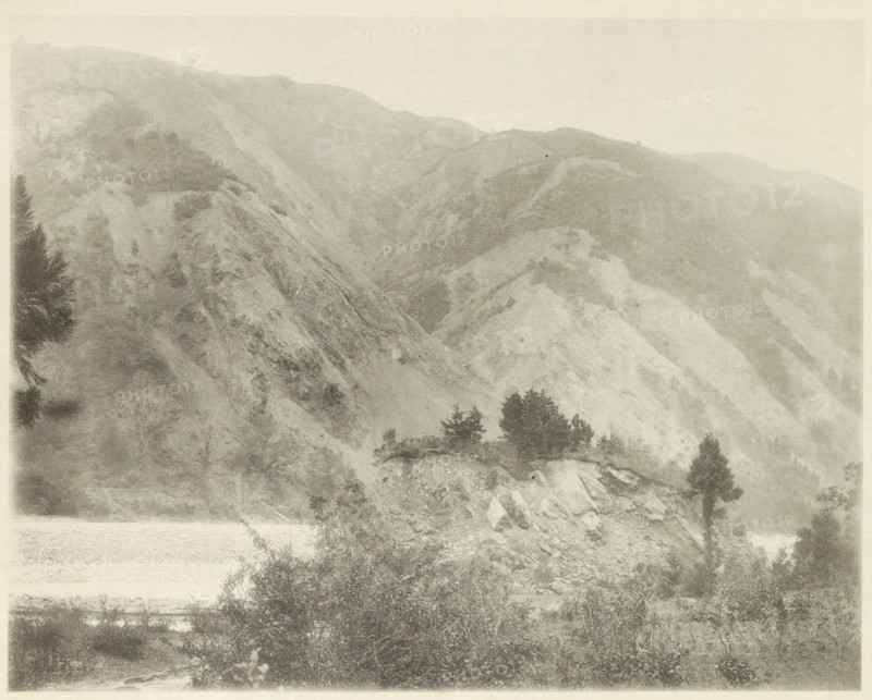Landslides in the Neo Valley in Japan after an earthquake, page, photomechanical print, Japan, cliché maker: Kazumasa Ogawa, after 1891-10-28 - in or before 1892, photographer, paper, collotype, photoprint, height 227 mm x width 288 mm, landslide, consequences of an earthquake, Mino–Owari earthquake 1891, A wide, monochrome landscape showing steep, rocky hills and ridges with sparse vegetation, several clusters of dark trees on a lighter rocky outcrop, dense bushes and shrubs in the foreground, and layered slopes fading into the misty background.