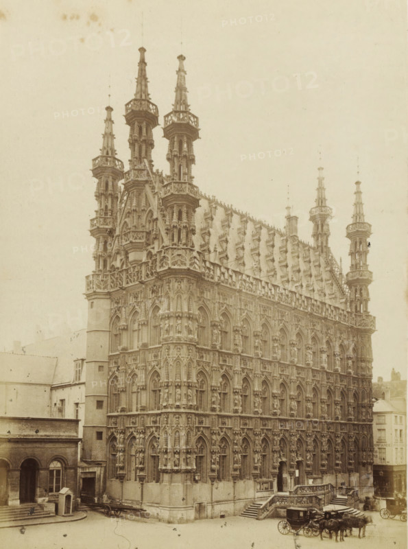 Hôtel-de-ville de Louvain, City Hall of Leuven, photograph, page, Louvain, c. 1862 - c. 1872, photographer, paper, albumen print, albumendruk, height 201 mm x width 145 mm, Photo on page 35., townhall, façade (of house or building), Stadhuis (Leuven), A large ornate stone building with multiple tall spires and pinnacles rises from a street, its façade covered in gothic arches, niches, and sculpted figures. The roofline features a steeply pitched section with numerous decorative dormers and finials, and crenellated balustrades run along the upper levels. At ground level a set of stone steps and an entrance with carved railings are visible, and a carriage with horses is parked on the street beside the building. Adjacent lower buildings with plain facades and arched doorways flank the ornate structure, and the scene is captured in a monochrome, aged photograph style.
