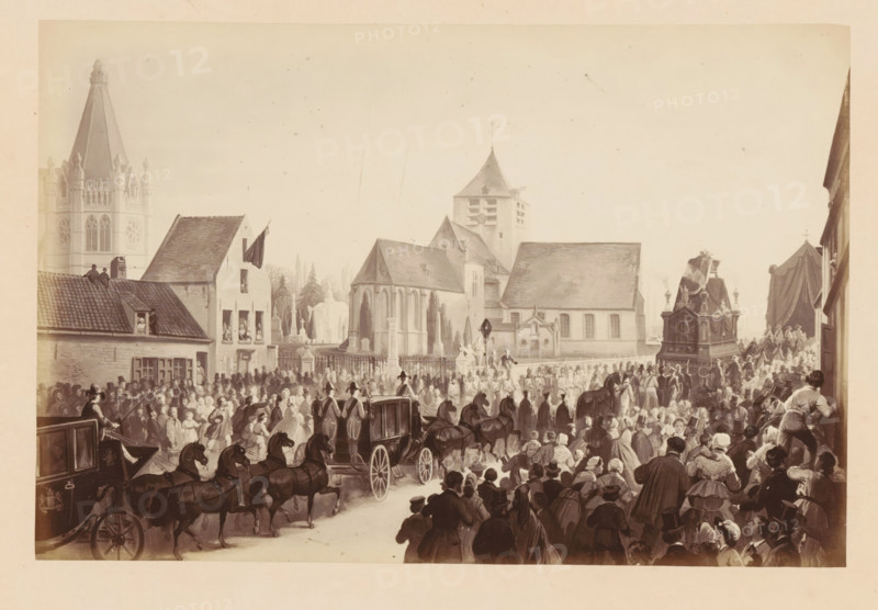 Cortège Funèbre - à son arrivée près de l'Eglise, Photo reproduction of a design of the funeral procession of King Léopold I of Belgium upon arrival at the church in Laeken, photograph, reproduction, This photo is part of a cover with fourteen photos., inscription: 'A Laeken.', photographer: Ghémar Frères, Brussels, after design by anonymous, c. 1861 - in or before 1866, Ghémar Frères, photographer, after design by, paper, albumen print, albumendruk, height 167 mm x width 249 mm, Person, Leopold I (king of the Belgians), cortege, funeral procession, king, Laeken, Period, 1865-12, A crowded street scene with many people gathered outdoors among buildings and churches, a large carriage drawn by multiple horses moving through the crowd, figures wearing coats and hats throughout, groups of onlookers clustered near building windows and rooftops, a procession including an ornately decorated platform draped with fabric and attended by people, stone church buildings with pitched roofs and a tow...