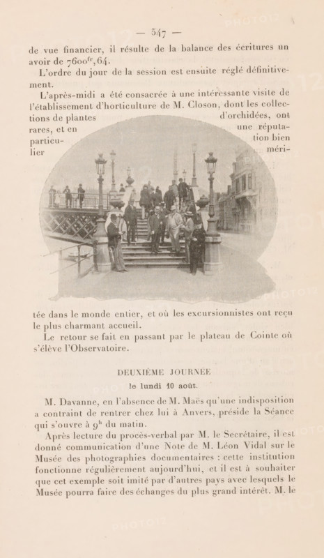 Members of the Union International de Photographie on a staircase in Liège, page, photomechanical print, 1896, paper, autotypie, height 67 mm x width 90 mm, historical persons (portraits and scenes from the life), staircase, A faded page with printed columns of text surrounding a central oval photograph showing a group of people standing and sitting on a set of stone steps leading up to a bridge or elevated walkway; the photograph includes decorative lamp posts and railings, several men in period clothing and hats clustered on the stairs and landing, a few figures standing on the bridge beyond, and buildings visible along a street to the right; the page has a worn, yellowed appearance and the photograph is slightly grainy and washed out.