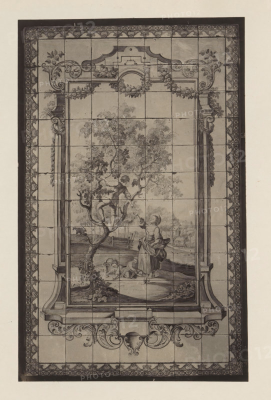 Tile wall of apple picking in the house of Antonin Terme, photograph, page, Liège, c. 1880 - in or before 1885, photographer, paper, platinum process, height 210 mm x width 133 mm, interior of the house, art collection, art gallery, tiles, bricks, building material, A tall rectangular artwork composed of square tiles framed by a patterned border is visible. The central scene shows a leafy tree with a figure perched among its branches and a standing figure nearby reaching upward while holding a wide-brimmed hat and a basket-like object. At the base of the tree two smaller figures sit on the ground near a basket. Architectural elements resembling columns and ornate scrollwork frame the central image, with decorative flourishes along the top and bottom margins. The image is monochromatic with shading that defines foliage, figures, and ornamental details, and faint grid lines where the tiles meet are visible across the entire surface.