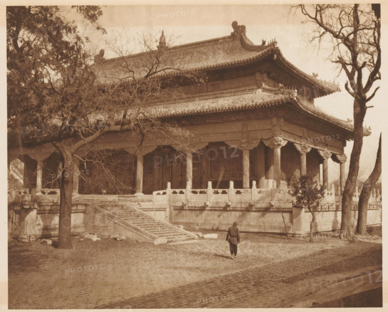 Temple in Beijing, page, photomechanical print, photographer: Donald Mennie, Beijing, cliché maker: anonymous, c. 1915 - in or before 1920, paper, rotogravure, height 203 mm x width 250 mm, places and objects of worship, non-Christian religions, A sepia-toned photograph of a large traditional building with a multi-tiered tiled roof and ornate eaves, raised on a stone platform with carved balustrades and a wide flight of stone steps leading up to a colonnaded veranda, leafless tree branches partially obscuring the upper structure, mature trees flanking the building, a cobbled foreground, and a solitary person standing near the base of the steps facing the building.