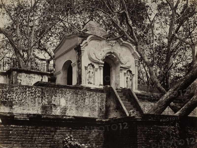 Second Flight of Steps Leading to the Sacred Bo Tree., Steps leading to the sacred bodhi tree in Anuradhapura, album page, photograph, Part of Album with 50 photos of a trip through Southeast Asia., photographer: Charles T. Scowen & Co., Anuradhapura, c. 1875 - c. 1880, South Asia, paper, albumen print, height 218 mm x width 279 mm, temple, shrine, Hinduism, Buddhism, Jainism, An ornate stone structure with a curved, decorative facade sits atop a weathered brick platform, accessed by a narrow flight of stone steps; the facade features sculpted niches containing standing figures and arched openings, flanked by pilasters and ornamental scrollwork, while trees with spreading branches and dense foliage surround and partially frame the building, and a metal railing runs along a raised area behind the structure.