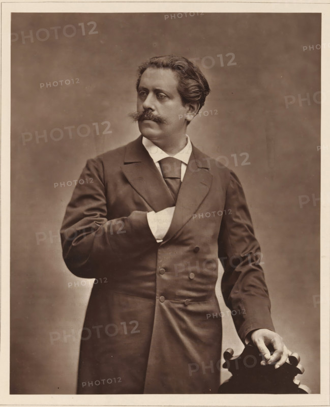 Paul de Cassagnac. Ne le 2 decembre 1842, a La Guadeloupe, Portrait of Paul de Cassagnac, page, photomechanical print, inscription: '126, boul. Magenta.-Paris.', photographer: Charles Louis Klary, cliché maker: Goupil & Cie., c. 1876 - in or before 1879, paper, Woodburytype, Woodburytypepie, height 228 mm x width 185 mm, Person, Paul de Cassagnac, journalist, reporter, A sepia-toned portrait of a man shown from the thighs up wearing a dark double-breasted coat with wide lapels and a light-colored shirt and tie, his left hand tucked inside his coat and his right hand resting on the carved top of a wooden chair; he has wavy hair swept back, a prominent mustache, and is looking slightly to his left against a plain, softly textured background.