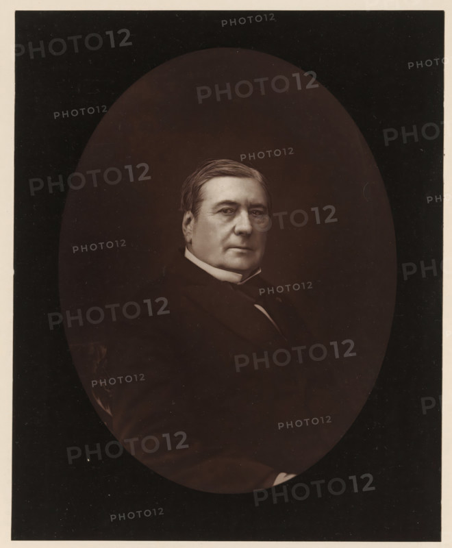 Portrait of Eugène Labiche, Eugène Labiche. Ne a Paris, le 6 mai 1815, page, photomechanical print, inscription: '126, boul. Magenta.-Paris.', photographer: Ferdinand Mulnier, cliché maker: Goupil & Cie., c. 1876 - in or before 1879, paper, Woodburytype, Woodburytypepie, height 228 mm x width 184 mm, Person, Eugène Labiche, portrait of a writer, A sepia-toned oval portrait of a middle-aged man shown from the chest up against a dark rectangular background, with neatly combed hair, a high collar, and a dark suit; he faces slightly to his left with a neutral expression, and the oval vignette softens the edges of his shoulders and torso.