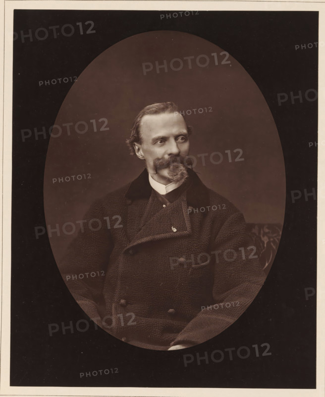 Cham. Ne a Paris, le 26 janvier 1819, mort a Paris, le 6 septembre 1879, Portrait of Charles Amédée de Noé, page, photomechanical print, inscription: '126, boul. Magenta.-Paris.', photographer: Ferdinand Mulnier, cliché maker: Goupil & Cie., c. 1876 - in or before 1879, paper, Woodburytype, Woodburytypepie, height 230 mm x width 186 mm, Person, Cham, portrait, self-portrait of graphic artist, caricatures (human types), A sepia-toned oval portrait of a seated man with a neatly groomed mustache and pointed goatee, wearing a textured double-breasted coat with a high collar and a visible shirt collar underneath, his head turned slightly to the viewer's left, the background dark and plain with a faint patterned cushion visible at the right edge.