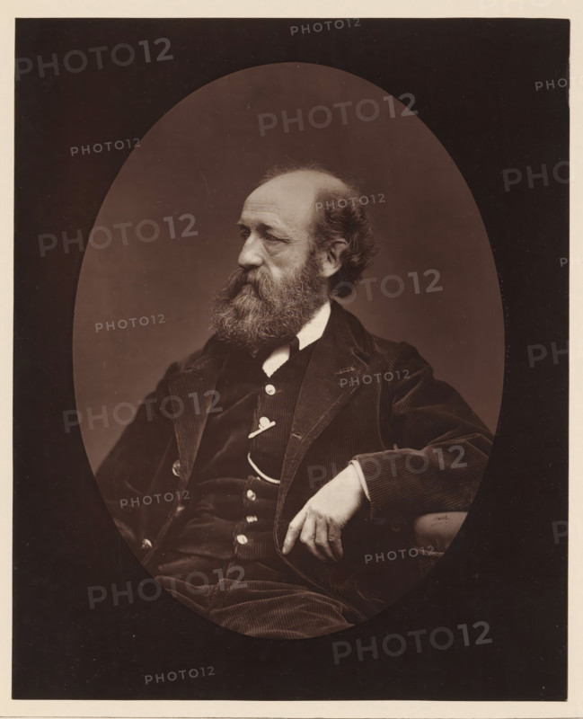 Edmond Morin. Ne au Havre, le 26 mars 1824, Portrait of Edmond Morin, page, photomechanical print, inscription: '126, boul. Magenta.-Paris.', photographer: Étienne Carjat, cliché maker: Goupil & Cie., c. 1876 - in or before 1879, paper, Woodburytype, height 228 mm x width 186 mm, Person, Edmond Morin, portrait, self-portrait of artist, A sepia portrait of a seated older man shown in an oval frame against a dark rectangular background, turned in three-quarter profile to his left, with a full beard and thinning hair, wearing a dark corduroy jacket and waistcoat with visible buttons and a light shirt collar, his right arm resting on an armrest and his right hand relaxed with fingers slightly curled, the lighting highlighting facial texture and the fabric details of his clothing.